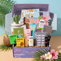 The TheraBox Paradise box features WARDA SKINCARE Dragonfruit & BHA Tropical Detox Clay Mask, BUFFOUT Callus Eraser Scrub Gel, ANIHANA Body Wash Bar, POOFY ORGANICS The Sunscreen Stick SPF 30+, YES TO Watermelon Refreshing Paper Mask, ANTHONY Lip Balm SPF 25, GLOW IS HERE Vitamin C Chewable, HAPPY SHOPPE Cactus Trinket Dish, and FAMILIUS X KATHRYN THOMPSON’s Drops of Awesome.