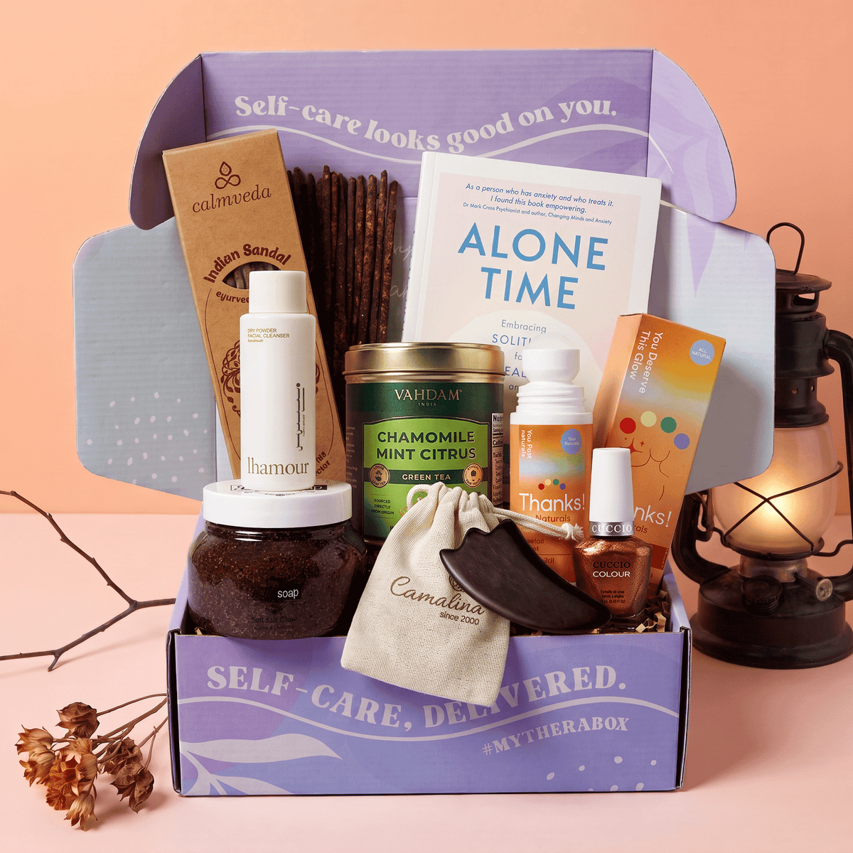 The TheraBox Autumn Embrace box features VAHDAM INDIA Chamomile Mint Citrus Tea, THANKS NATURALS Charmed by Chai Massage Oil Roll-On, LHAMOUR Dry Powder Facial Cleanser, HEALTH HEALING Wooden Gua Sha Tool, CUCCIO Higher Grounds Nail Polish, CALMVEDA Sandalwood Resin 24 Sticks, LOLA SOAP Soft Salt Glow – Jojoba and Lavender, and ROCKPOOL PUBLISHING’s Alone Time: Embracing Solitude for Health and Well Being.
