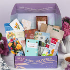 The TheraBox Full Bloom box features STONE STREET SOAPHOUSE Geranimo Body Scrub, THE AROMA SHOP Tea Tree Essence Mask 5-Pack, AYNIL CO. All Is Well Bracelet, FRESHCUT PAPER Mini Sorbet Roses, CUSHLA TEA Raw Pu-Erh & Jasmine Resin Tea, SENTIER Notes of Reverie Eau de Parfum, BOIRON USA Calendula Gel, and I KNOW COLLECTION The Bloom Deck Affirmation Cards.
