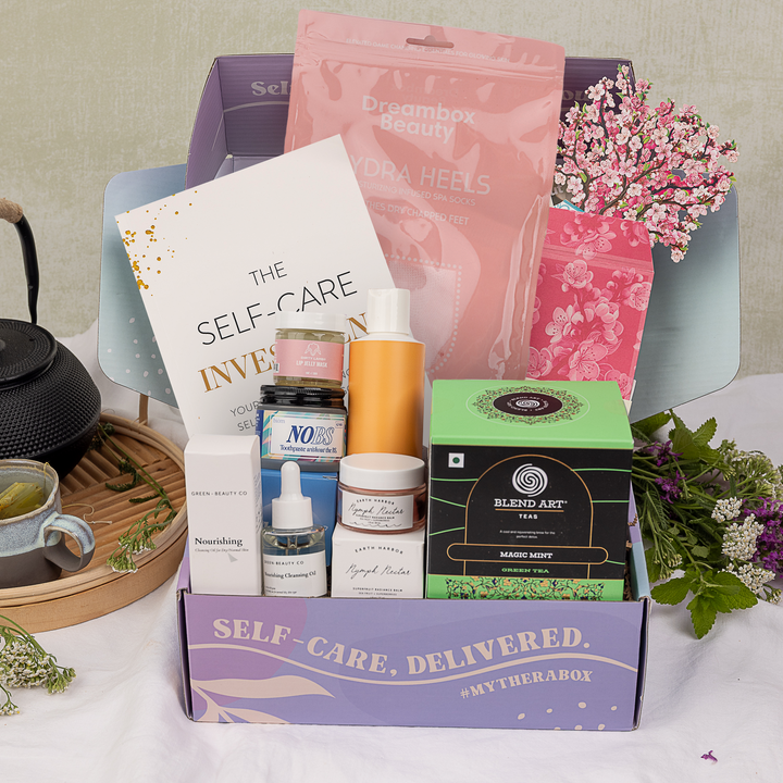 TheraBox Pampered Box featuring Earth Harbor Nymph Nectar Superfruit Radiance Balm, Green Beauty Co Nourishing Cleansing Oil, Cove Haircare All-In-One Hair Cream, Dream Box Beauty Hydrating Gel Infused Moisturizing Spa Socks, BIÖM Nobs Toothpaste Tablets, Dirty Lamb Lip Jelly Mask, Blend Art Teas Magic Mint Green Tea, Freshcut Papers Mini Cherry Blossoms Pop-Up Card and The Essence of Healing and GMichelle Wellness The Self-Care Investment Handbook