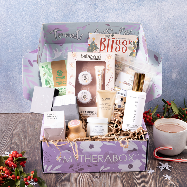 TheraBox Bliss box featuring Elements Truffles | Peppermint Hot Chocolate, Earth Harbor | Siren Silk Face Moisturizer, AHAVA | 24K Gold Mineral Mud Mask, Stone Candles | Oud Wood Room Spray, BellaPierre Cosmetics | Vanilla Lip Care Kit, Aminnah | Marshmallow Smores Bath Milk, AYNIL | Rose Quartz Wooden Eye Roller, MYNDLY | Values Deck