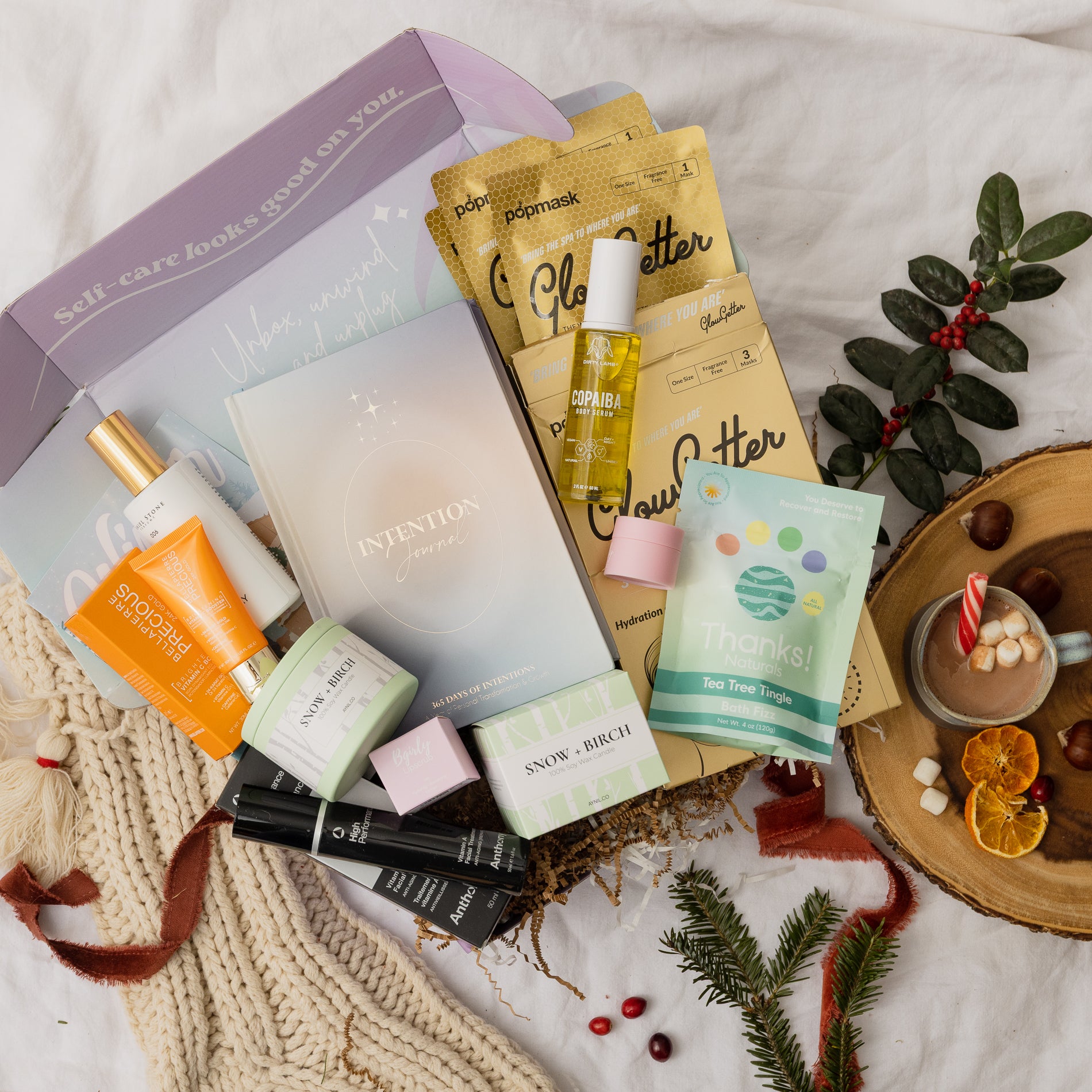 TheraBox Winter box features DIRTY LAMB Copaiba Body Serum, ANTHONY Vitamin A Facial Treatment, AYNIL Snow Birch Candle, THANKS NATURALS Tea Tree Tingle Bath Fizz, DANIEL STONE Winter Forest Room Spray, BGIRLY LIPSAUCE Toasted Marshmallow Lip Scrub, BELLÁPIERRE Brightening Vitamin C Booster Night-Time Serum, POPMASK Glowgetter 3-Pack, and RISE THROUGH LOVE 365 Intention Journal.