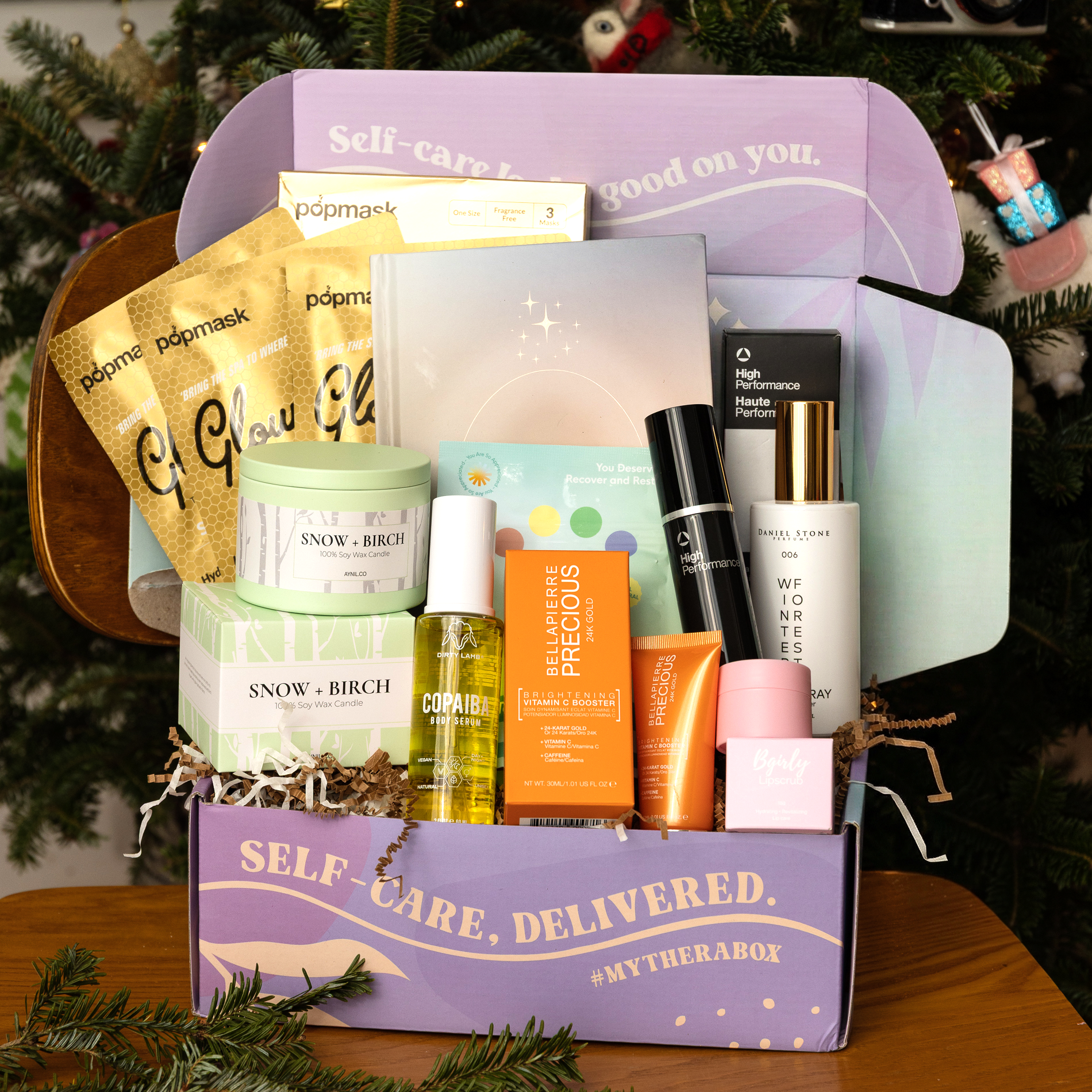 TheraBox Winter box features DIRTY LAMB Copaiba Body Serum, ANTHONY Vitamin A Facial Treatment, AYNIL Snow Birch Candle, THANKS NATURALS Tea Tree Tingle Bath Fizz, DANIEL STONE Winter Forest Room Spray, BGIRLY LIPSAUCE Toasted Marshmallow Lip Scrub, BELLÁPIERRE Brightening Vitamin C Booster Night-Time Serum, POPMASK Glowgetter 3-Pack, and RISE THROUGH LOVE 365 Intention Journal.